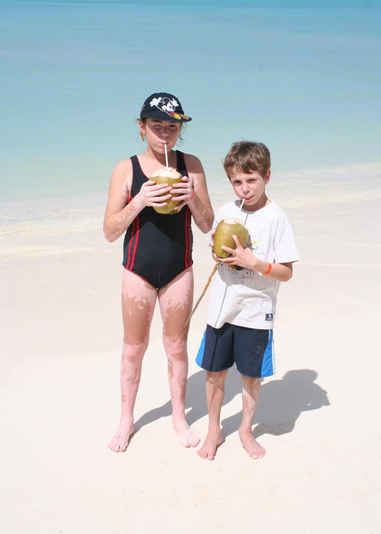 Aruba with Kids - 2 kids drinking from coconuts at the beach