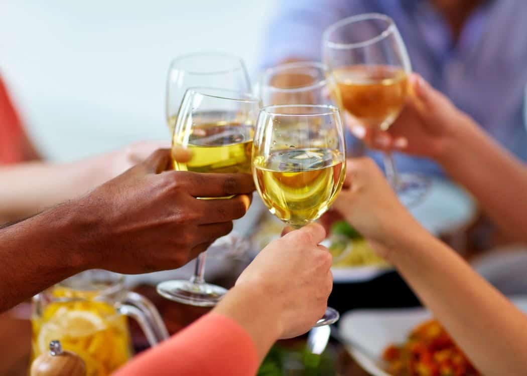People clinking white wine glasses at table